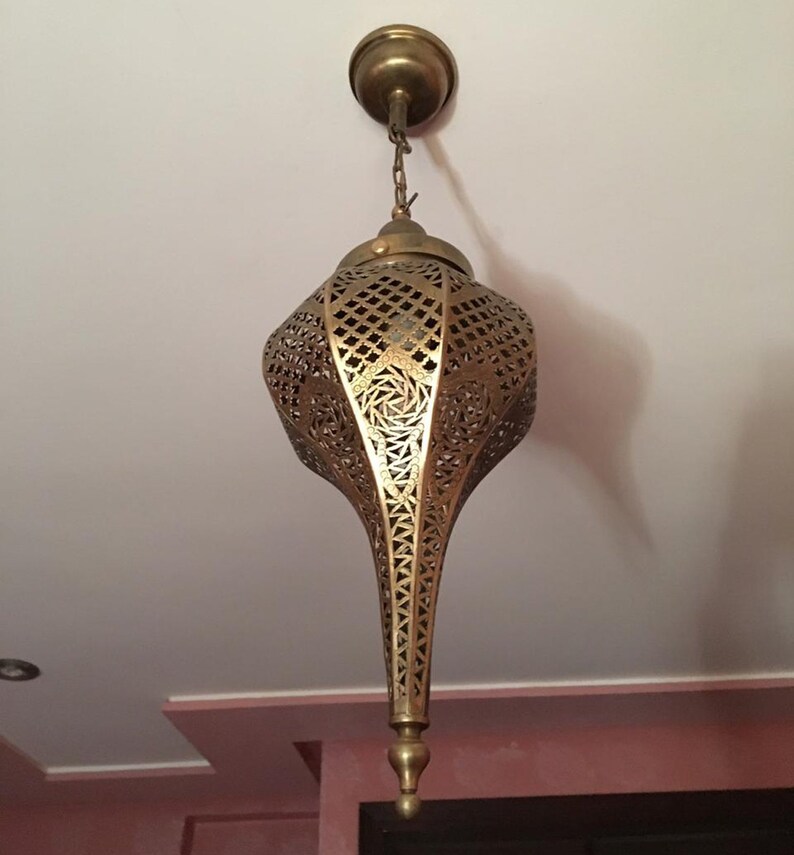 May include: A gold metal pendant light fixture with intricate cut-out designs. The light fixture is shaped like a teardrop and hangs from a chain.