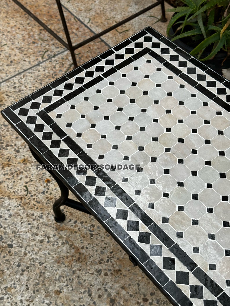 May include: A black and white Moroccan tile table with a geometric pattern. The table has a black metal frame and is sitting on a concrete surface.