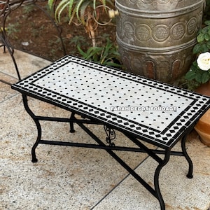 May include: A black metal table with a white and black mosaic tile top. The table has a decorative design on the legs and is sitting on a stone patio.