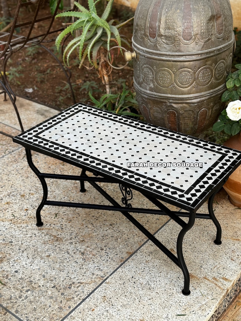 May include: A black metal table with a white and black mosaic tile top. The table has a decorative design on the legs and is sitting on a stone patio.