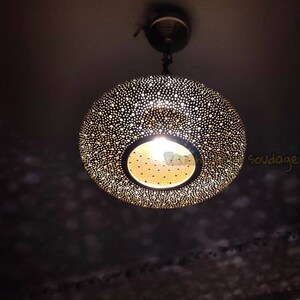 May include: A decorative pendant light fixture with a perforated, spherical shade. The shade is dark with numerous small holes, allowing light to filter through. The light source is visible at the bottom, creating a warm glow. The fixture hangs from the ceiling.