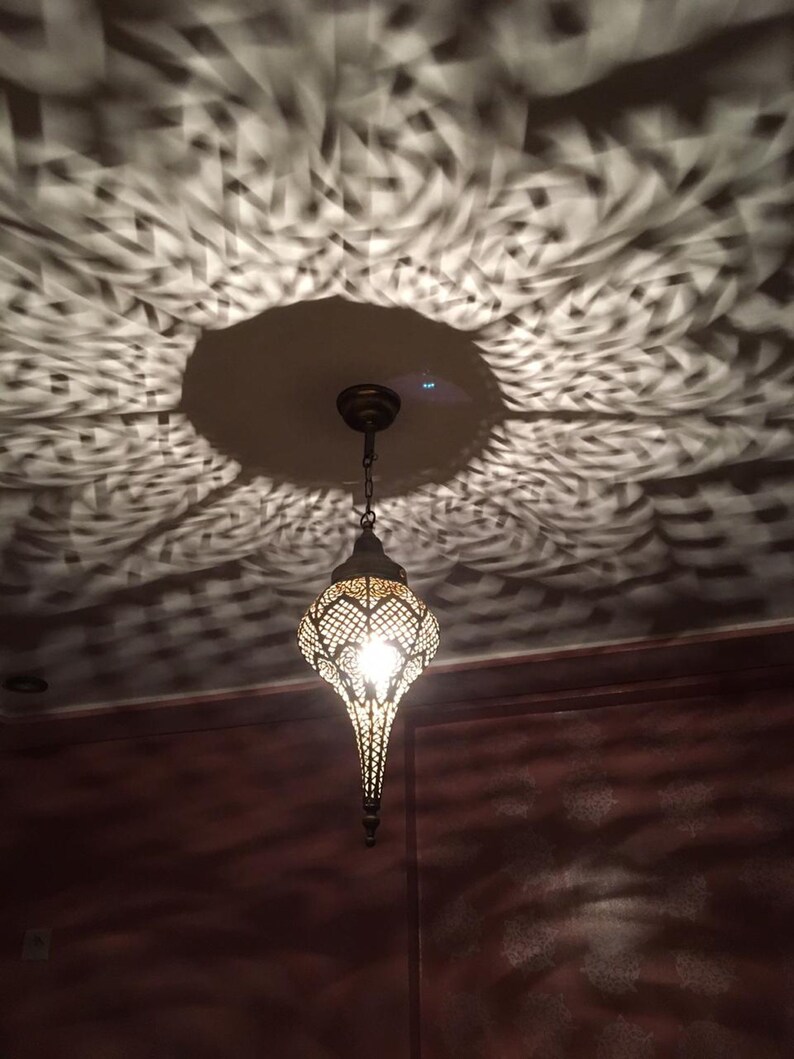 May include: A decorative metal pendant light fixture with a geometric design hangs from the ceiling, casting intricate shadows on the wall. The light fixture is made of brass and has a warm, inviting glow.