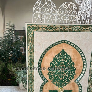 Puede incluir: Una fuente decorativa de azulejos con un dise&ntilde;o de mosaico verde y marr&oacute;n. La fuente presenta un arco tradicional marroqu&iacute; y intrincados patrones florales. El texto "FARAH DECOR SOUDAGE" es visible en la fuente.