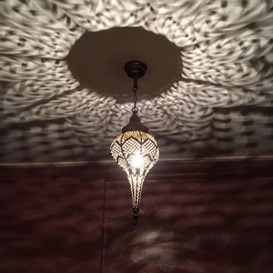 May include: A decorative metal pendant light fixture with a geometric design hangs from a ceiling. The light casts a patterned shadow on the ceiling.