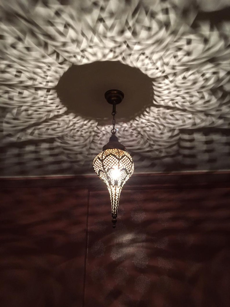 May include: A decorative metal pendant light fixture with a geometric design hangs from a ceiling. The light casts a patterned shadow on the ceiling.
