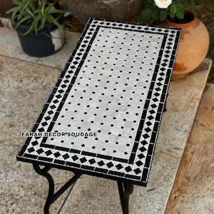 May include: A black and white Moroccan tile top coffee table with a black metal frame. The table has a geometric pattern of black and white squares and diamonds.