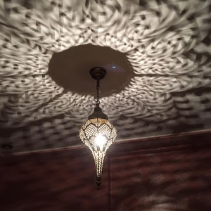 May include: A decorative metal pendant light fixture with a geometric design hangs from the ceiling. The light casts a patterned shadow on the ceiling.