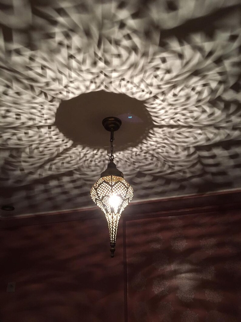May include: A decorative metal pendant light fixture with a geometric design hangs from the ceiling. The light casts a patterned shadow on the ceiling.