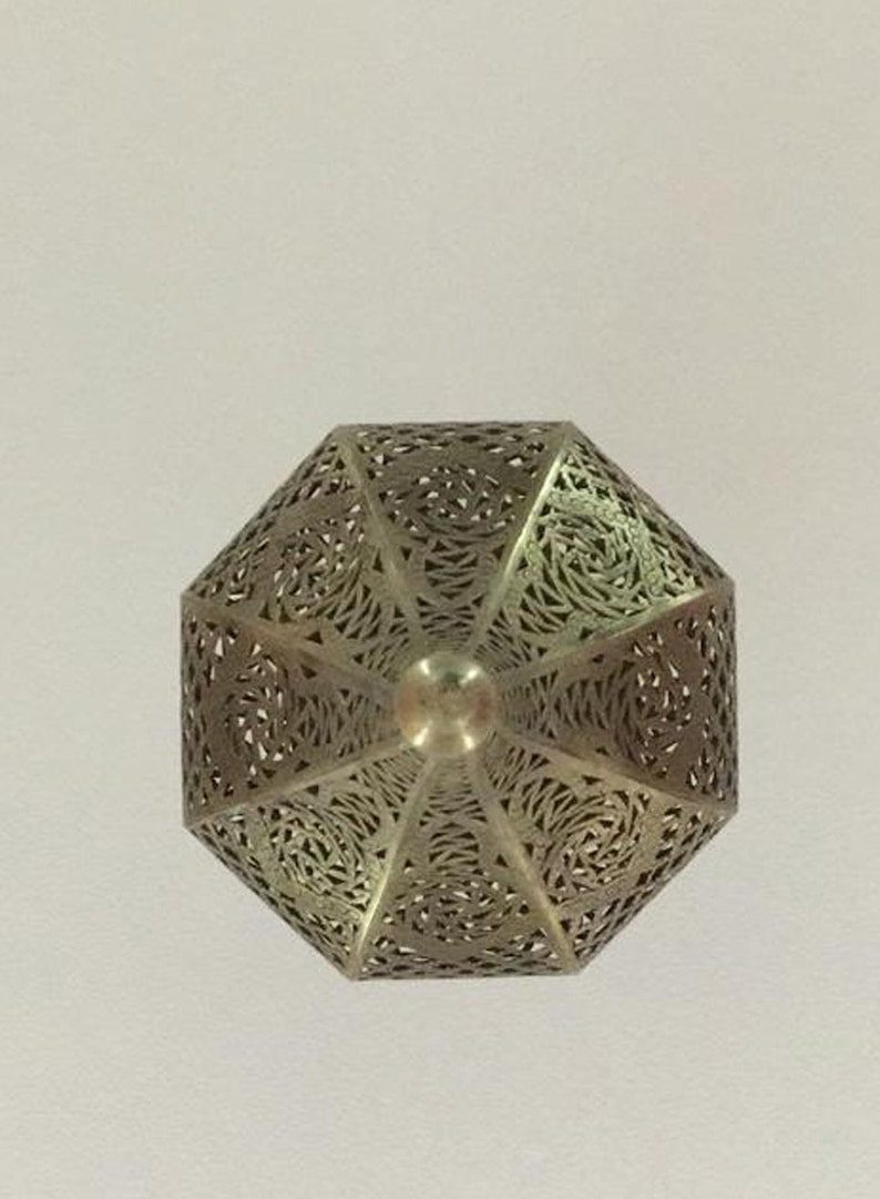 May include: A silver metal lantern with intricate cut-out designs. The lantern is shaped like a pyramid with a pointed top.
