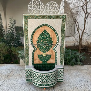 Puede incluir: Una fuente de azulejos verdes y blancos con un dise&ntilde;o tradicional marroqu&iacute;. La fuente tiene una peque&ntilde;a cuenca y un ca&ntilde;o. El texto "FARAH DECOR SOUDAGE" es visible en la fuente.