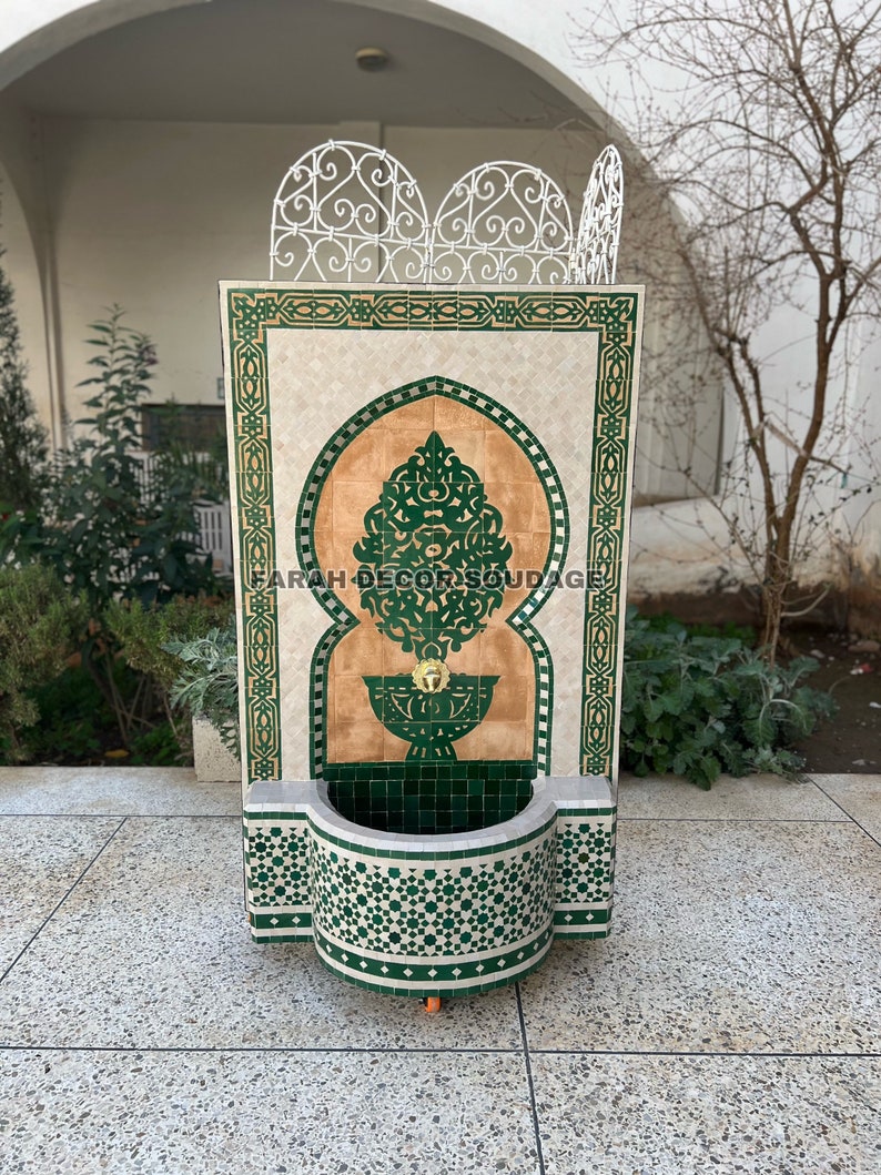 Puede incluir: Una fuente de azulejos verdes y blancos con un dise&ntilde;o tradicional marroqu&iacute;. La fuente tiene una peque&ntilde;a cuenca y un ca&ntilde;o. El texto "FARAH DECOR SOUDAGE" es visible en la fuente.