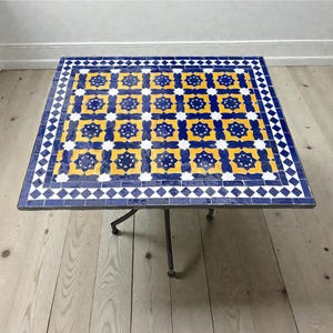 May include: Square mosaic tile table with a blue, yellow, and white geometric pattern. The table has a dark metal frame and legs. The tabletop is approximately 30 inches square.