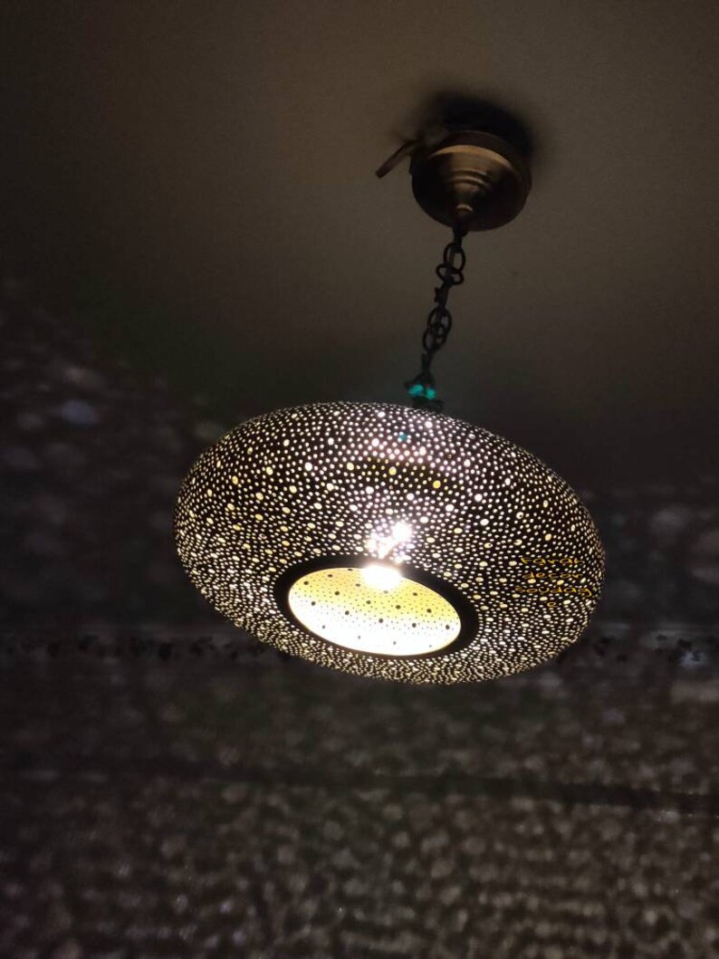 May include: A decorative, hanging pendant light with a perforated, bronze-colored shade. The light fixture is suspended from a chain and ceiling mount. The shade's design casts a pattern of light and shadow.