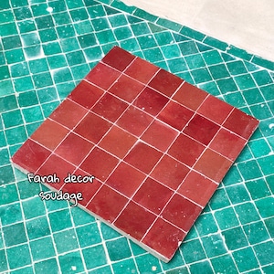 May include: A close-up of a red tile sheet, made of small square tiles, on a green tile background. The text "Farah decor soudagge" is written in green on the red tile sheet.