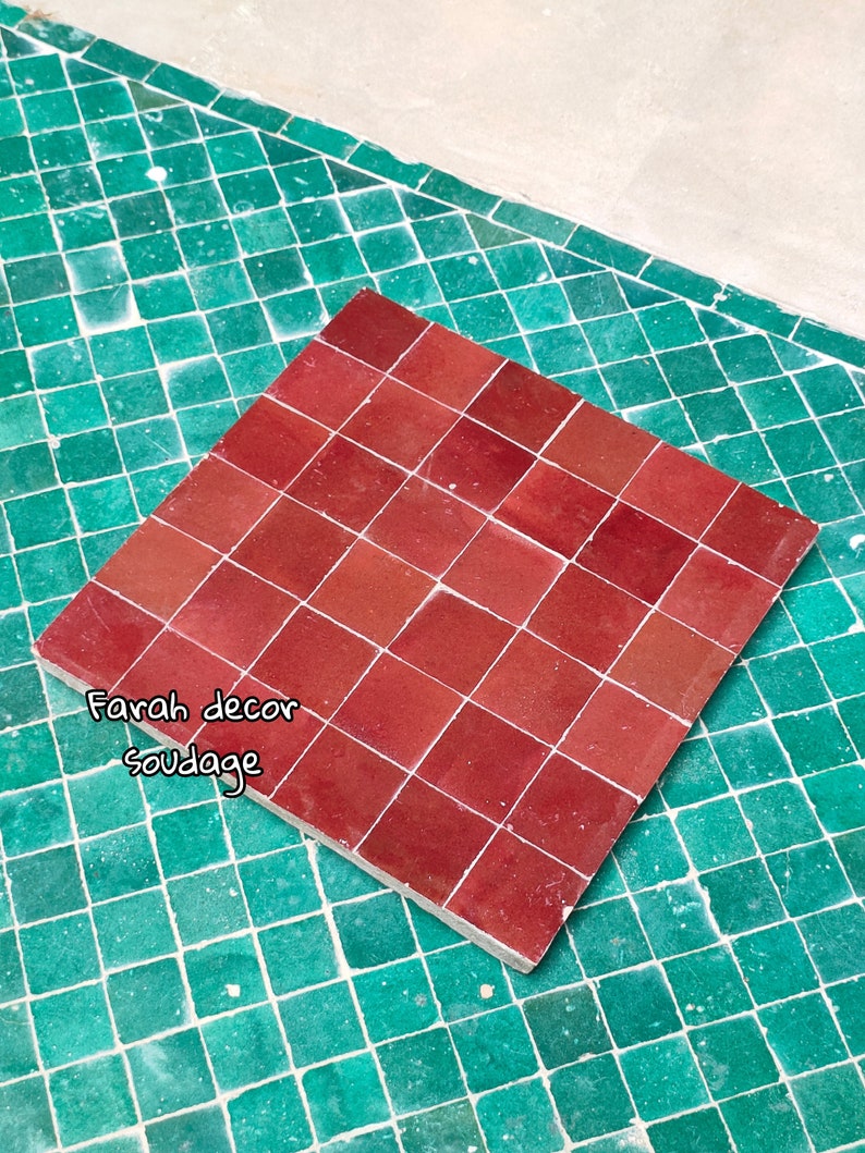 May include: A close-up of a red tile sheet, made of small square tiles, on a green tile background. The text "Farah decor soudagge" is written in green on the red tile sheet.