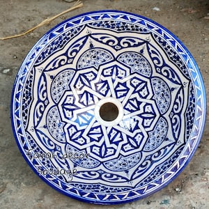 Puede incluir: Un lavabo de cerámica blanca con un patrón geométrico azul y blanco. El lavabo es redondo y tiene un agujero en el centro para el desagüe.