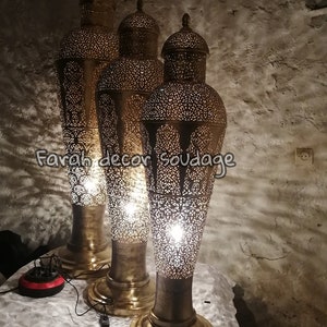 K&ouml;nnte beinhalten: Drei verzierte goldene Stehlampen aus Metall mit filigranen Ausschnitten. Die Lampen sind beleuchtet und strahlen ein warmes Licht aus. Der Text "Farah decor soudage" ist im Bild sichtbar.