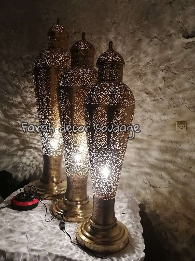 K&ouml;nnte beinhalten: Drei verzierte goldene Stehlampen aus Metall mit filigranen Ausschnitten. Die Lampen sind beleuchtet und strahlen ein warmes Licht aus. Der Text "Farah decor soudage" ist im Bild sichtbar.