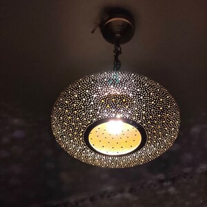 May include: A decorative, hanging pendant light with a perforated metal shade. The shade is a dark color with numerous small holes, allowing light to shine through. The light fixture is suspended from the ceiling by a chain.