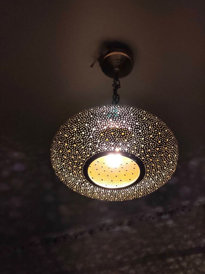 May include: A decorative, hanging pendant light with a perforated metal shade. The shade is a dark color with numerous small holes, allowing light to shine through. The light fixture is suspended from the ceiling by a chain.