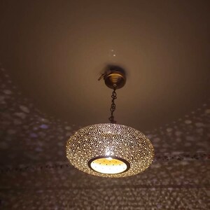 May include: A brass-colored, round pendant light fixture with a perforated design. The light casts a pattern of dots on the ceiling and walls. The fixture is suspended from the ceiling by a chain.