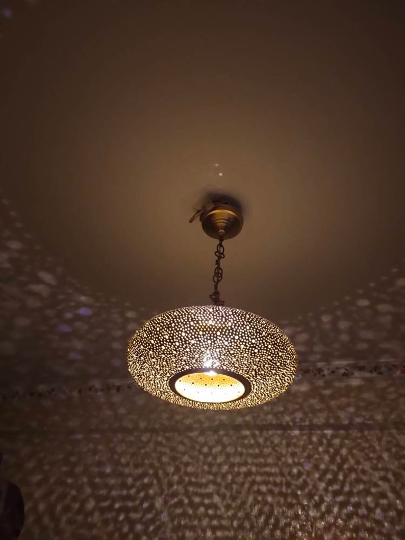 May include: A brass-colored, round pendant light fixture with a perforated design. The light casts a pattern of dots on the ceiling and walls. The fixture is suspended from the ceiling by a chain.