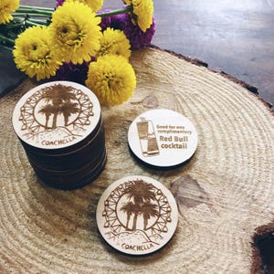 May include: Wooden coasters with a laser-engraved design of the Coachella Ferris wheel and palm trees. One coaster says "Good for one complimentary Red Bull cocktail."