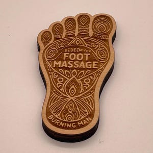 May include: Wooden foot-shaped token with intricate designs and the text "Redeem for Foot Massage Burning Man".