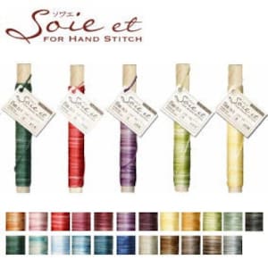 Pode incluir: Seis carretéis de fio Soie et para costura à mão. Os carretéis são de madeira e têm um rótulo com o nome da marca. As cores do fio são verde, vermelho, roxo, verde e amarelo.