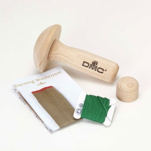 Puede incluir: Un hongo de zurcido de madera con un hilo verde e instrucciones para zurcir. El hongo está etiquetado como "DMC" y el hilo también está etiquetado como "DMC".