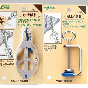 以下が含まれることがあります： キルティング用の縫製工具2点。最初の工具は、青い紐が取り付けられた銀色の金属製クランプ。2つ目の工具は、青いハンドルが付いた銀色の金属製クランプ。両方の工具のパッケージは白地に黒文字。パッケージのテキストには、「クローバー」と「かけはり」と「机上くけ台」と記載されています。