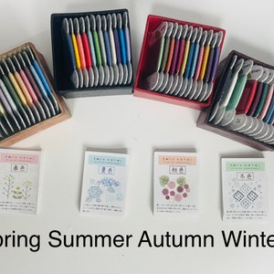 May include: Several boxes of colourful embroidery floss are displayed, each containing a different palette of threads. The image shows four boxes, each with a unique colour scheme. Below the boxes are four cards with Japanese text and seasonal illustrations. The text "Spring Summer Autumn Winter" is at the bottom.