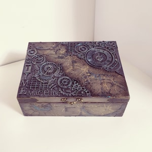 May include: A dark brown wooden box with a steampunk design. The box is decorated with metal gears, clock faces, and the words "TIME MACHINE".