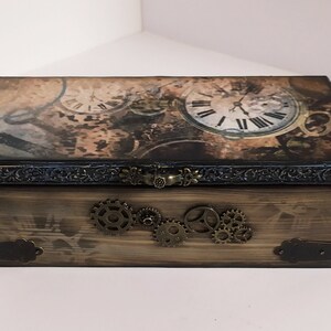 May include: A rectangular wooden box with a steampunk design. The lid features clock faces and gears, with a dark brown and tan color scheme. The box has metal gears and corner accents, and a clasp closure.