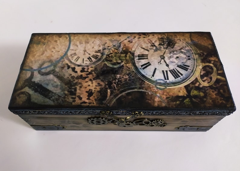 May include: Wooden box with a steampunk design featuring clock faces and gears. The box has a hinged lid and a metal clasp. The top of the box has a vintage-style print with clock faces and gears.