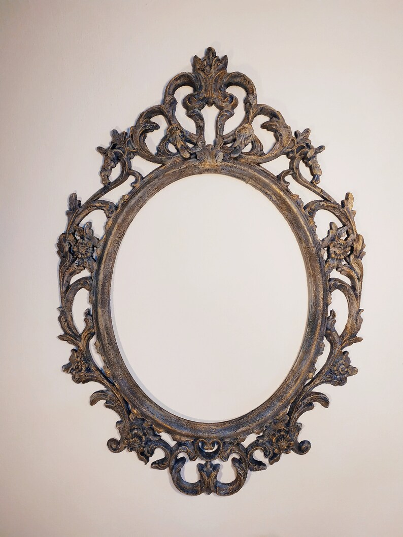 May include: An ornate oval-shaped picture frame with a distressed gold finish. The frame has intricate details and a decorative top.