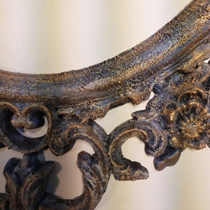 May include: A decorative, ornate, oval-shaped picture frame with a distressed, aged finish. The frame is painted in a dark blue and gold color scheme. The frame has a detailed, intricate design with a textured surface.
