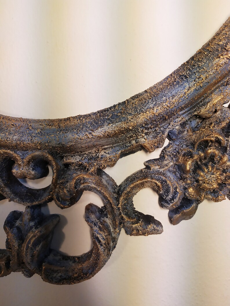 May include: A decorative, ornate, oval-shaped picture frame with a distressed, aged finish. The frame is painted in a dark blue and gold color scheme. The frame has a detailed, intricate design with a textured surface.