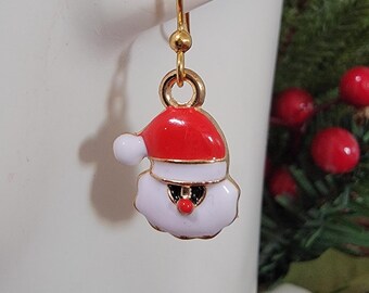 Puede incluir: Un pendiente dorado de Papá Noel con gorro rojo y barba blanca. El pendiente es un accesorio festivo para las fiestas, perfecto para Navidad. El pendiente cuelga de un gancho dorado.