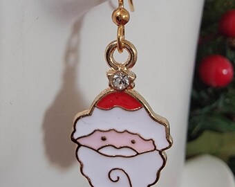 Puede incluir: Pendiente colgante de Papá Noel en tono dorado. El pendiente presenta una cara festiva de Papá Noel con gorro rojo, barba blanca y mejillas rosadas. Una pequeña gema transparente está engastada encima del dije de Papá Noel. El pendiente es para orejas perforadas.