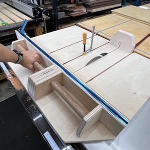 K&ouml;nnte beinhalten: Nahaufnahme eines Tischkreiss&auml;gen-Zubeh&ouml;rs aus Holz mit einer blauen Schiene und einem Holzgriff. Das Zubeh&ouml;r ist an einer Tischkreiss&auml;ge mit einem Kreiss&auml;geblatt befestigt.