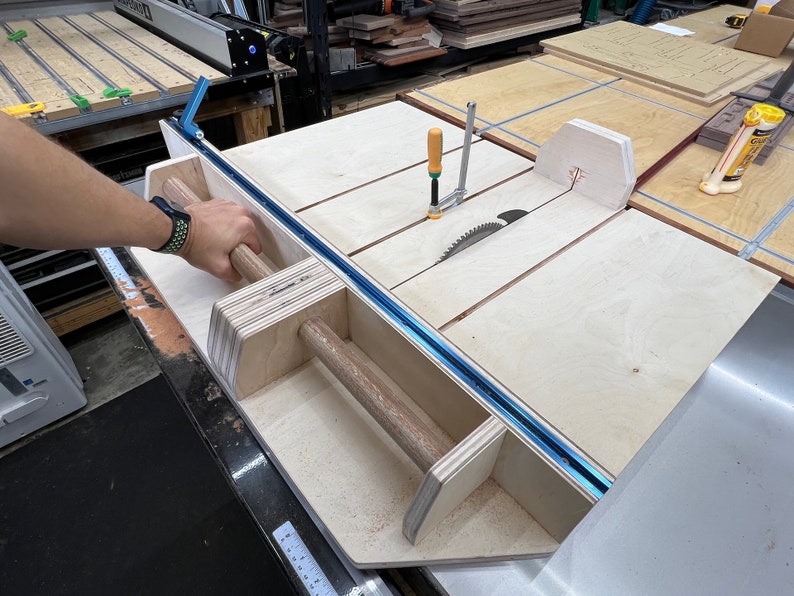 K&ouml;nnte beinhalten: Nahaufnahme eines Tischkreiss&auml;gen-Zubeh&ouml;rs aus Holz mit einer blauen Schiene und einem Holzgriff. Das Zubeh&ouml;r ist an einer Tischkreiss&auml;ge mit einem Kreiss&auml;geblatt befestigt.