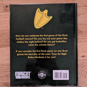 May include: The back cover of a book titled "Twas the Night Before Duckmas" with a green and yellow duck foot print logo. The book is published by Mascot Books and features a "Genuine College Product" seal.