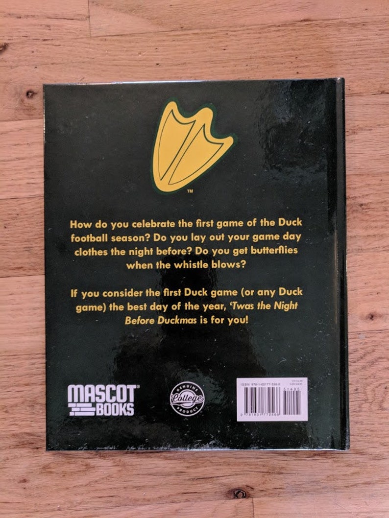 May include: The back cover of a book titled "Twas the Night Before Duckmas" with a green and yellow duck foot print logo. The book is published by Mascot Books and features a "Genuine College Product" seal.