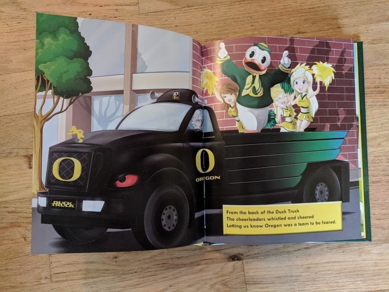 May include: A black truck with a large "O" for Oregon on the front grill. The truck is decorated with green and yellow accents. Cheerleaders are standing in the back of the truck, waving yellow pom-poms. The text "From the back of the Duck Truck The cheerleaders whistled and cheered Letting us know Oregon was a team to be feared." is printed below the image.