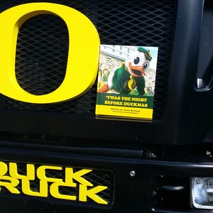 May include: A black truck with a yellow "O" on the front grill. The truck has a yellow "DUCK TRUCK" on the front bumper. A book titled "Twas the Night Before Duckmas" is attached to the grill.