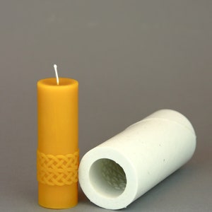 May include: A yellow candle with a braided design and a white wick, next to a white silicone candle mould.