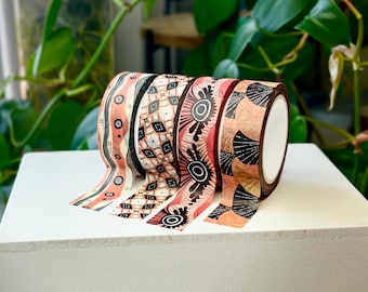 May include: Five rolls of patterned washi tape with black and orange designs on a white background. The tape is rolled up and stacked on top of each other.