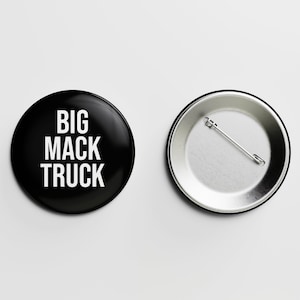 May include: A black button with the text "BIG MACK TRUCK" in white letters. The back of the button is silver with a safety pin.