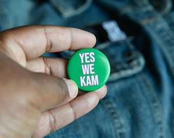 May include: A green button with the text "YES WE KAM" in white letters.